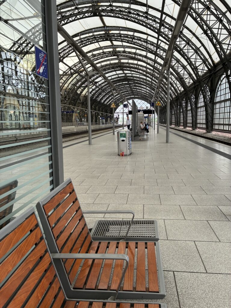Bilde av en perong på en overbygd jernbanestasjon med benker i forgrunnen.